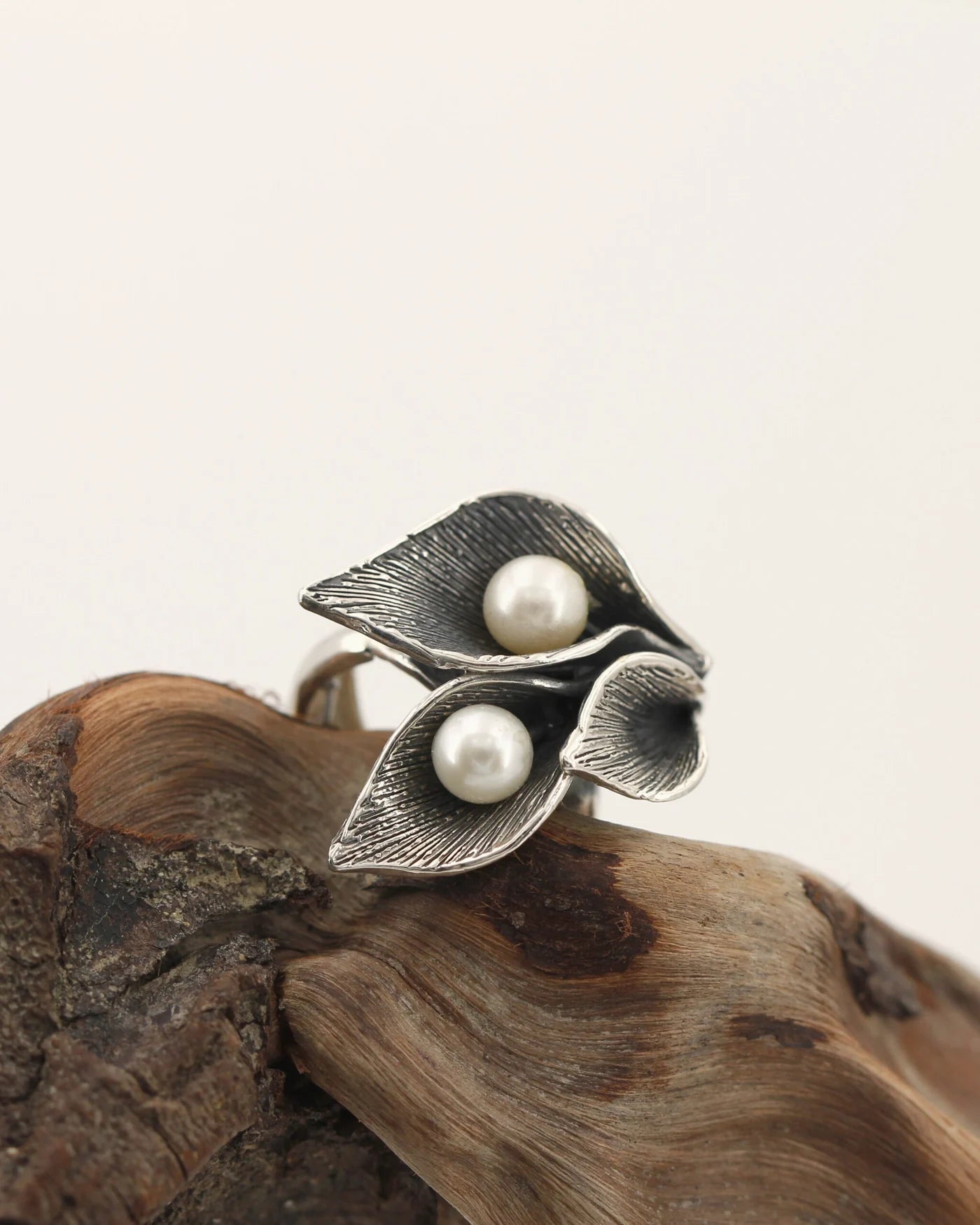Anello a tre calle in argento con perle d'acqua dolce, su un legno