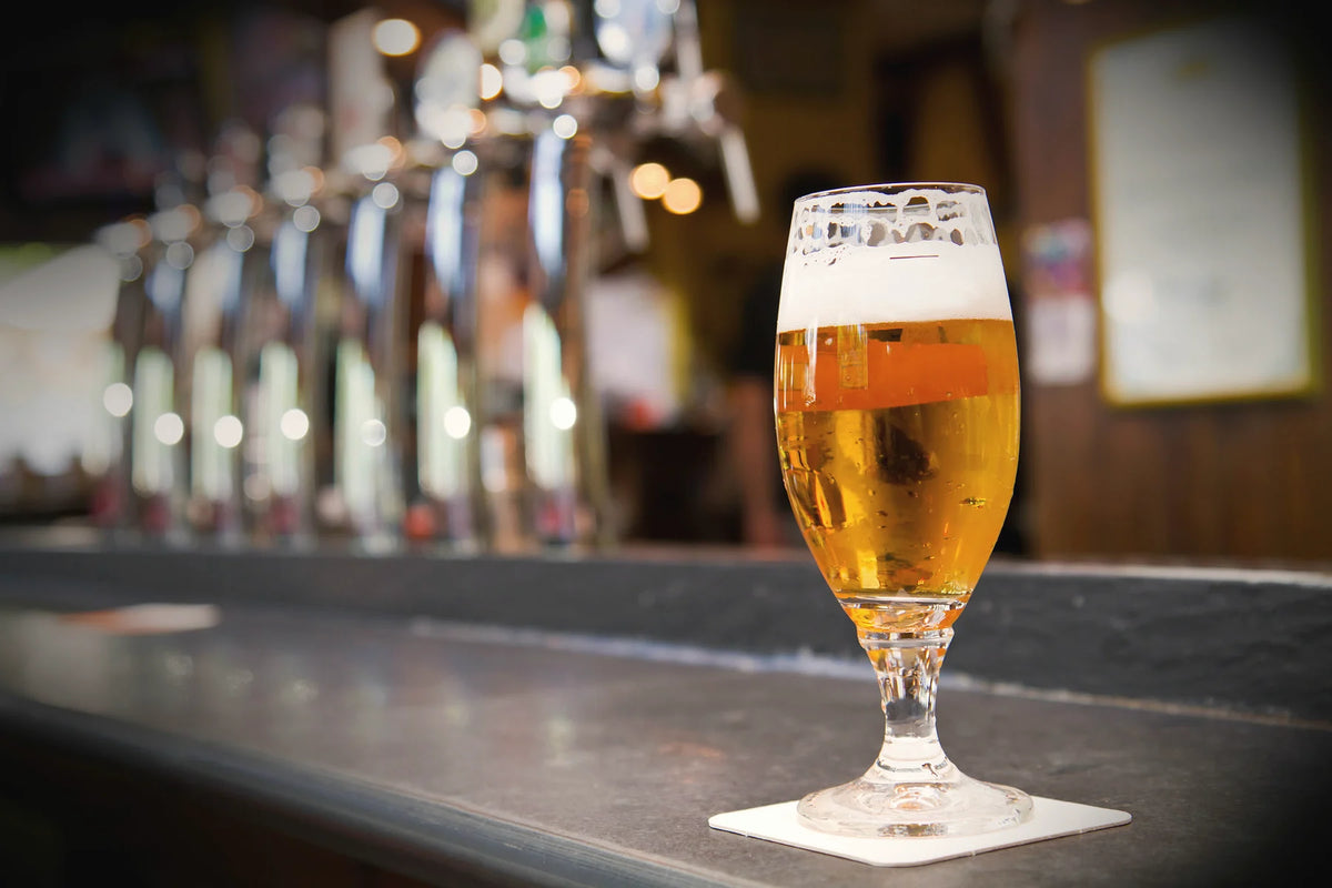 Un bicchiere di birra chiara sul bancone davanti alle spine
