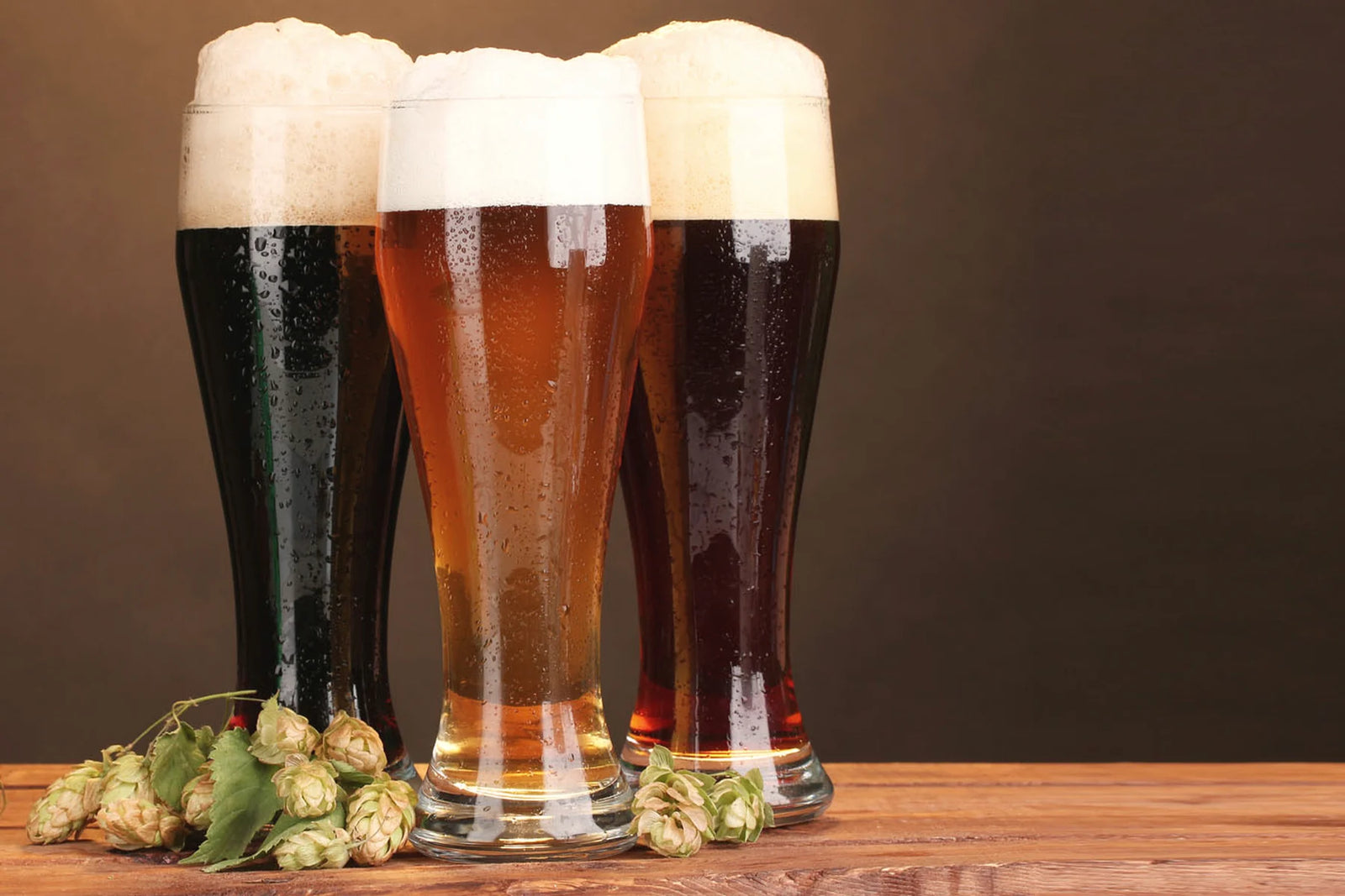 Tre bicchieri di birra scura, chiara e ambrata con coni di luppolo