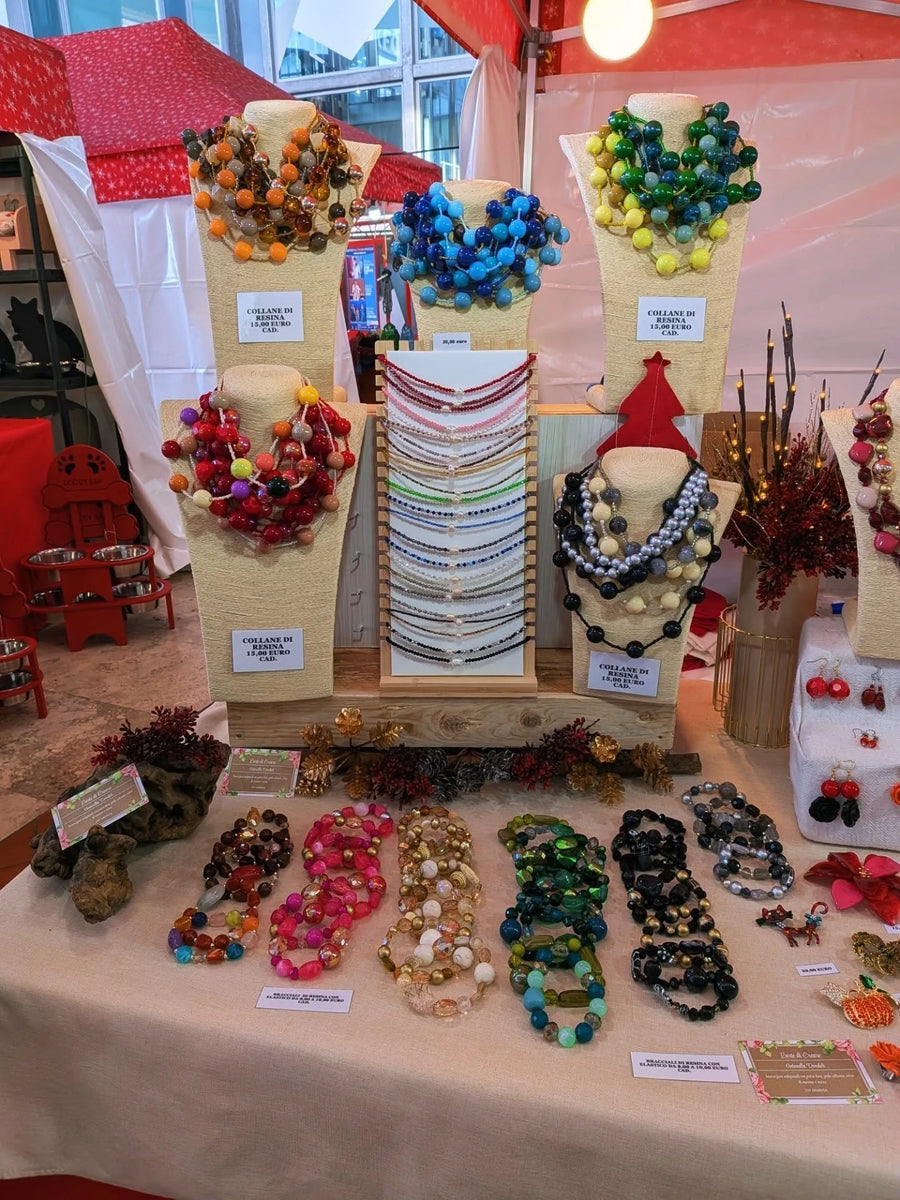 Il banco di L'ARTE DI CREARE a un mercatino: espositori pieni di collane, bracciali e orecchini in pietre colorate, con i cartellini dei prezzi.