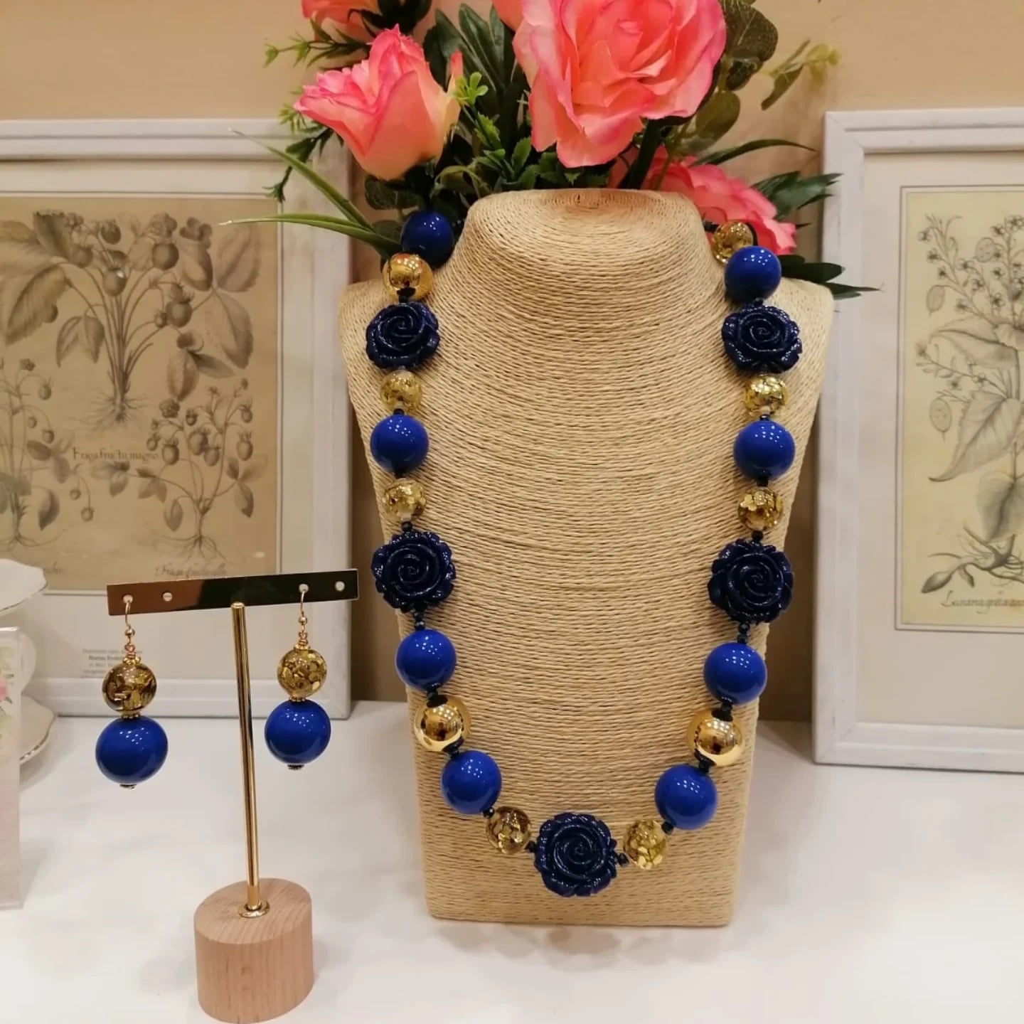 Dentro il negozio di Porretta Terme: un espositore di juta con una collana di pietre blu e oro, orecchini abbinati e fiori sullo sfondo.