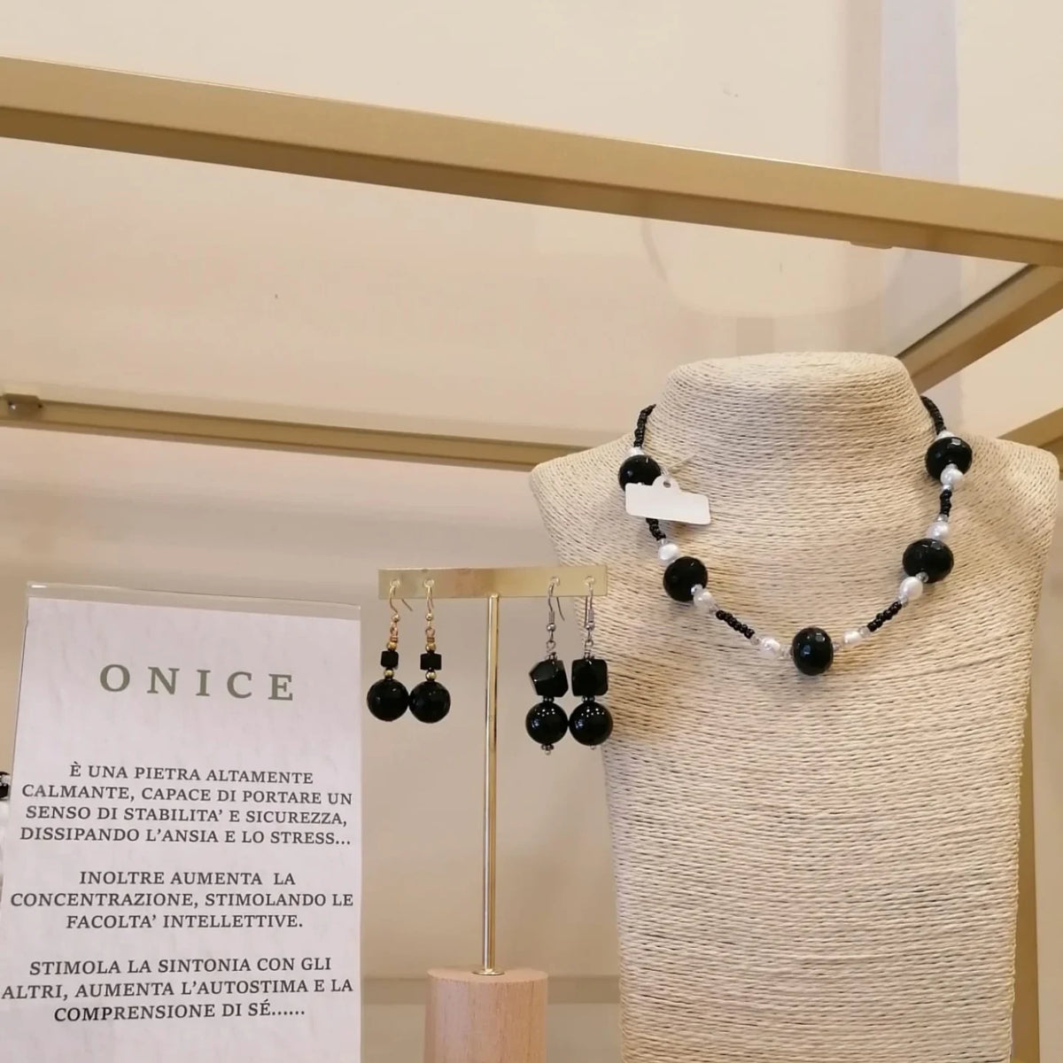 Una collana in onice nero e perle bianche con gli orecchini abbinati, accanto al cartoncino che spiega le proprietà dell'onice.