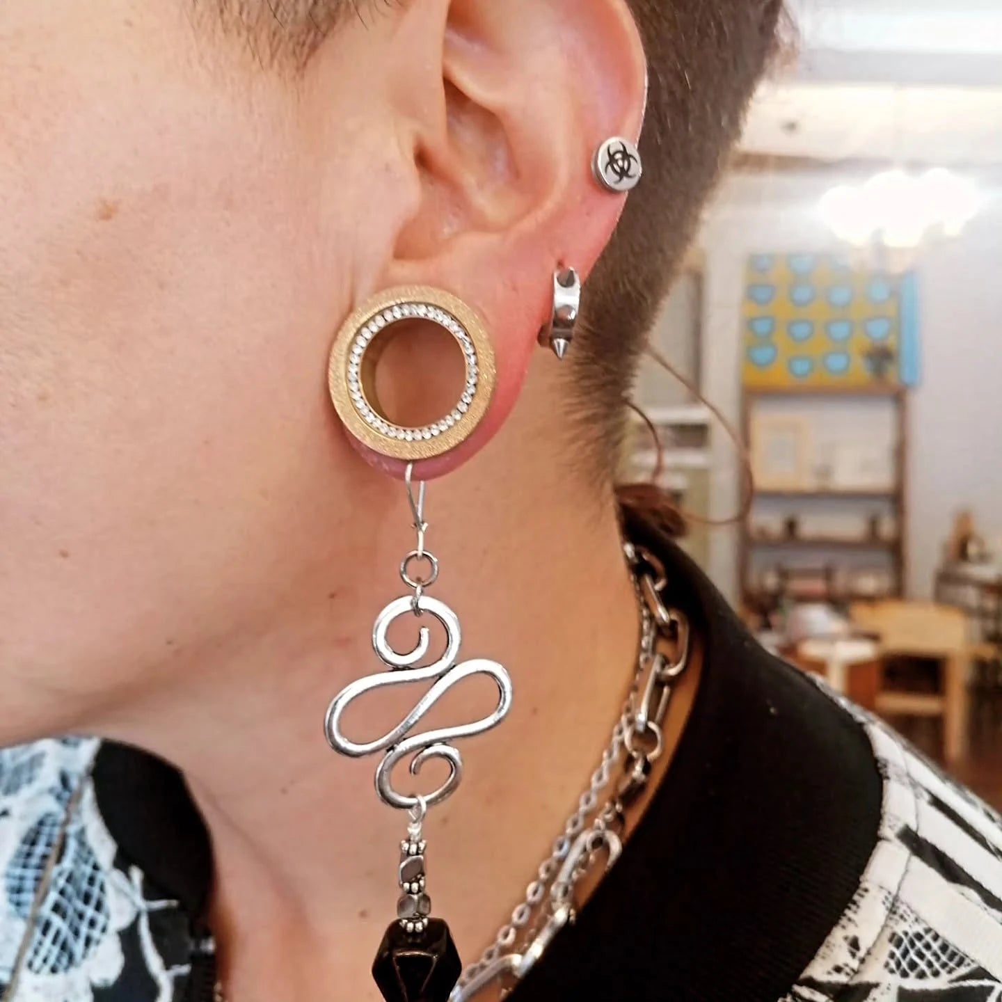 Un orecchino pendente indossato: perno tondo dorato, spirale d'argento lavorata a mano e goccia di pietra nera sfaccettata.