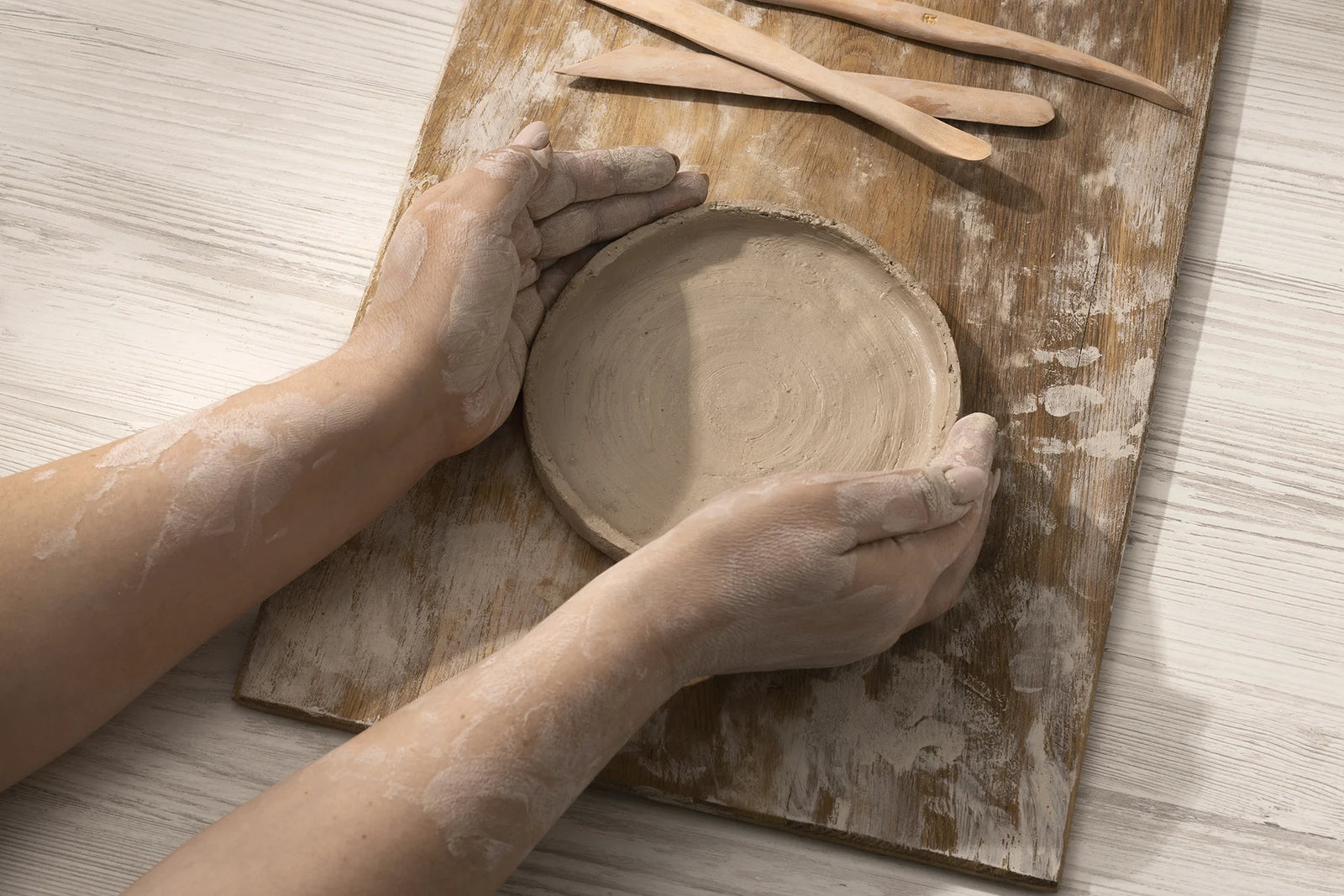 Mani che modellano un piatto d'argilla su una tavola di legno