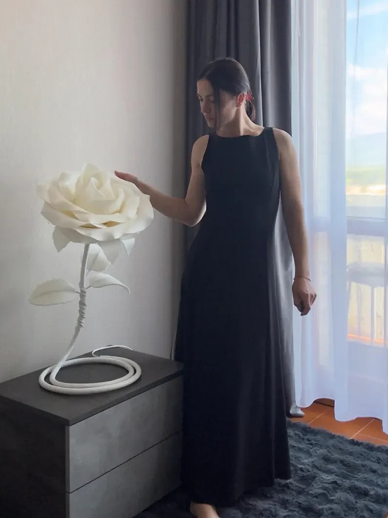 Una donna in abito lungo accanto a una piantana a forma di rosa bianca