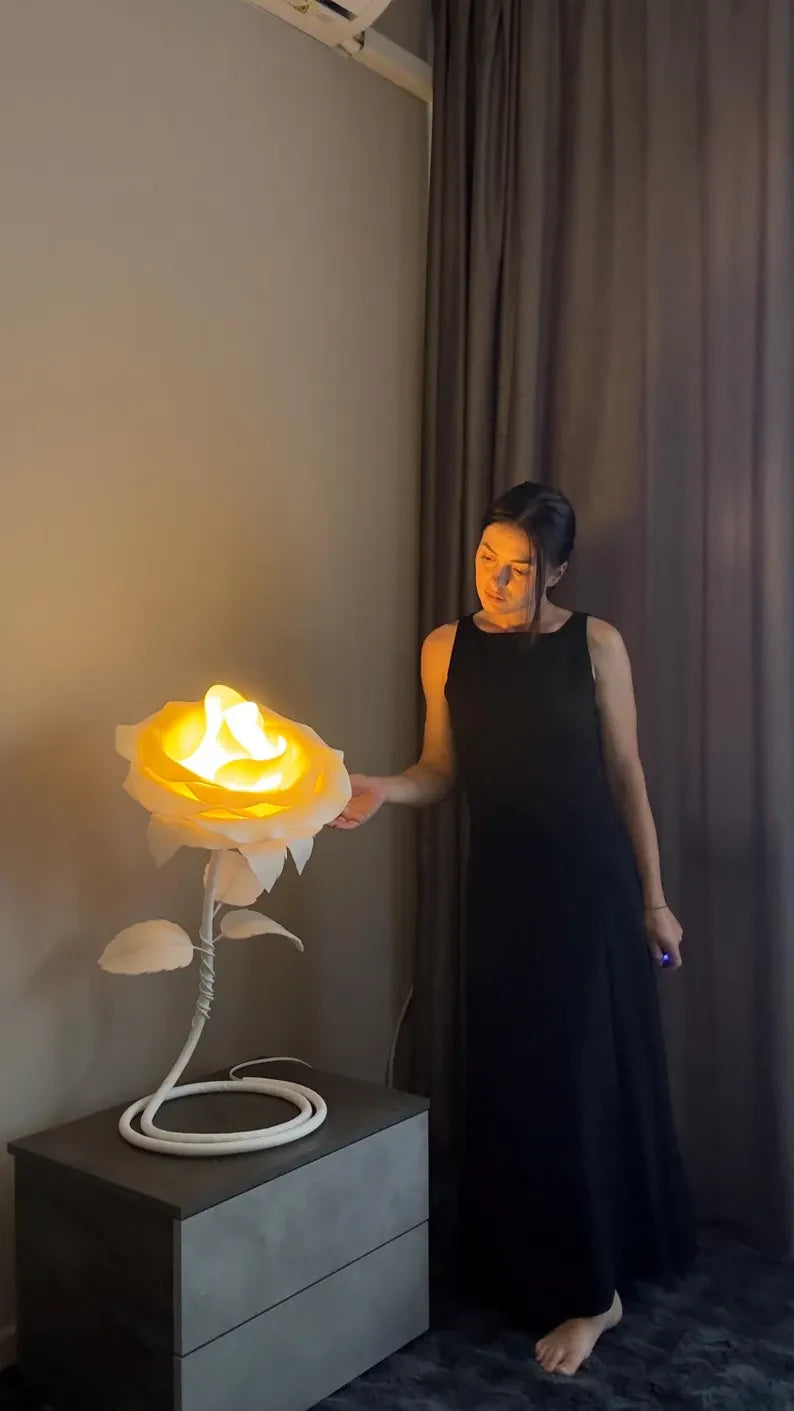 Una donna sfiora una lampada a forma di rosa accesa, in una stanza in penombra