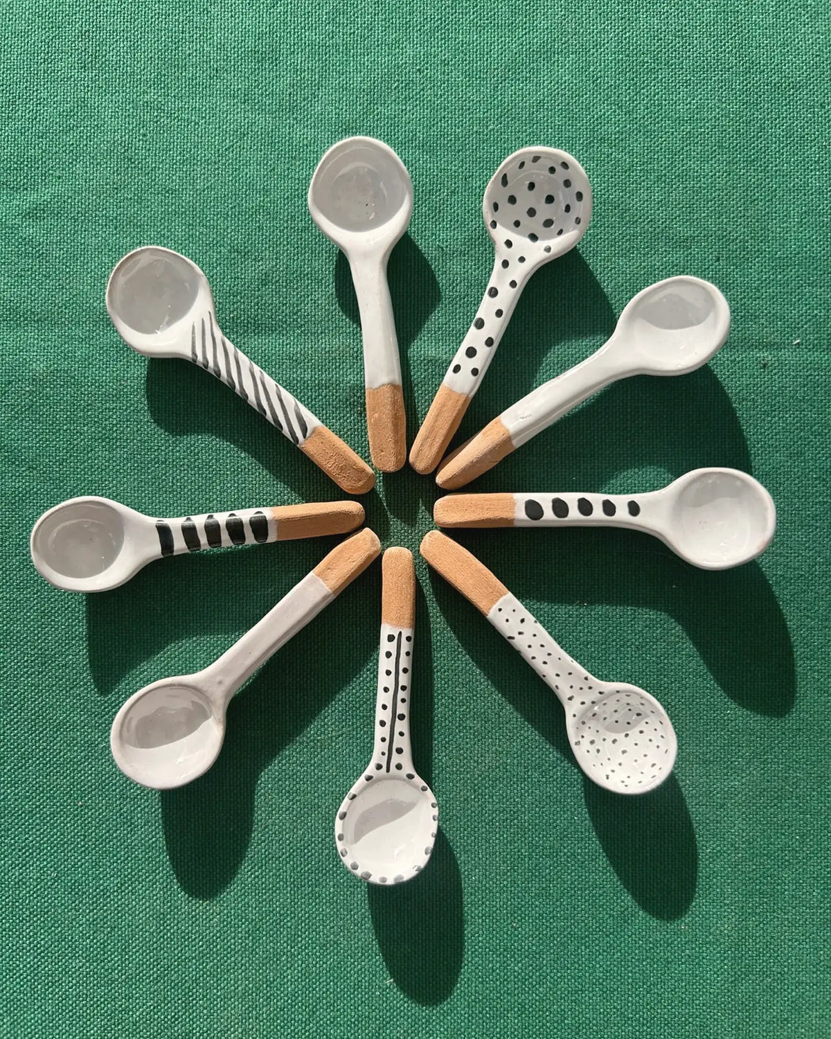 Nove cucchiai di ceramica disposti a raggiera, ogni manico decorato in modo diverso