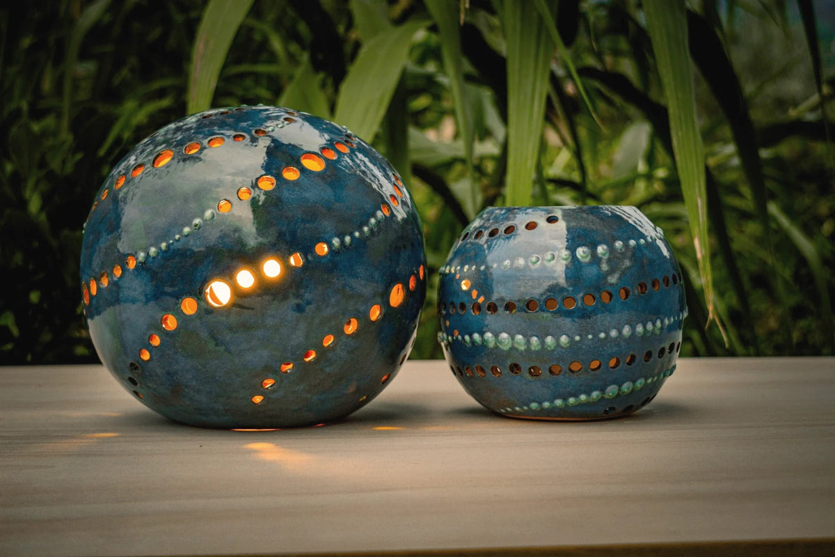 Due lampade in ceramica traforata accese al crepuscolo, la luce che esce dai fori