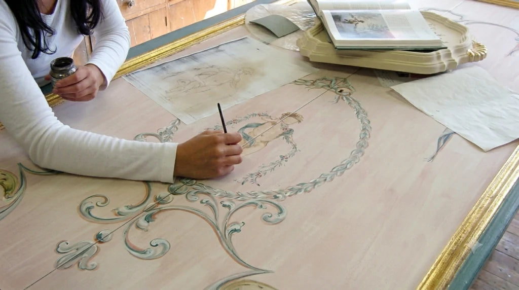 La decoratrice dipinge a pennello un pannello, con il disegno di riferimento accanto