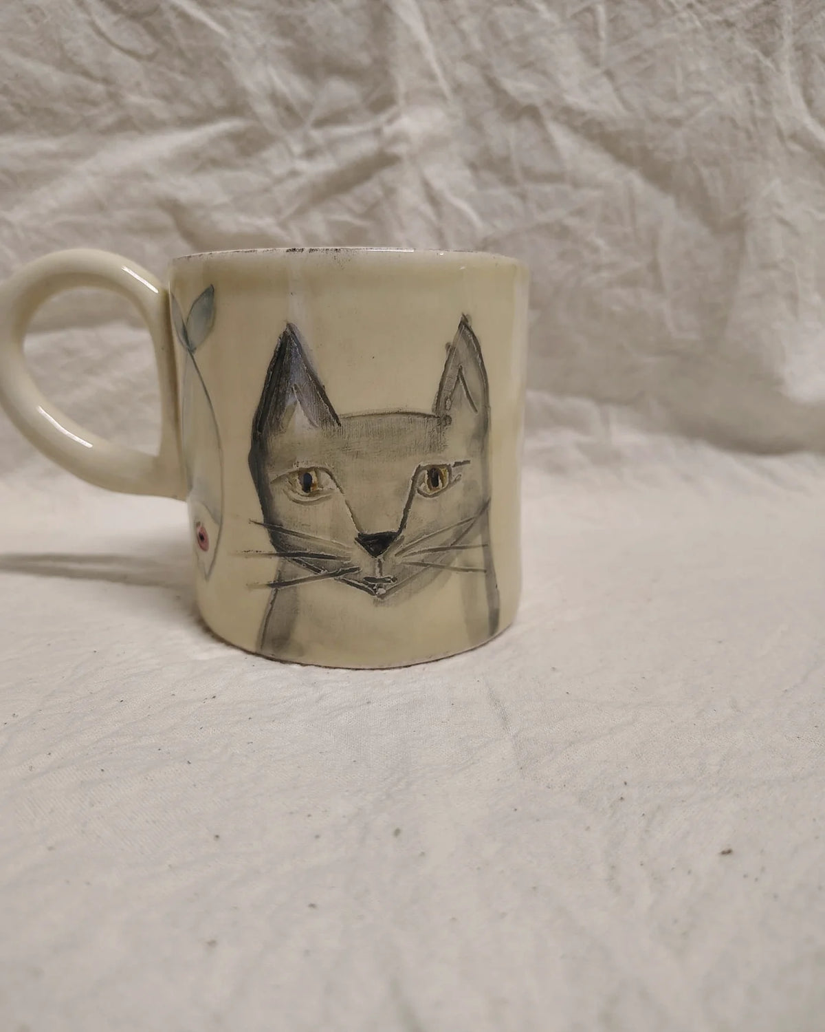 Tazza in ceramica con un gatto disegnato a grafite, su un telo di lino stropicciato
