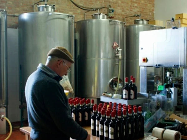 Un uomo al lavoro accanto ai serbatoi d'acciaio, con le bottiglie sul nastro